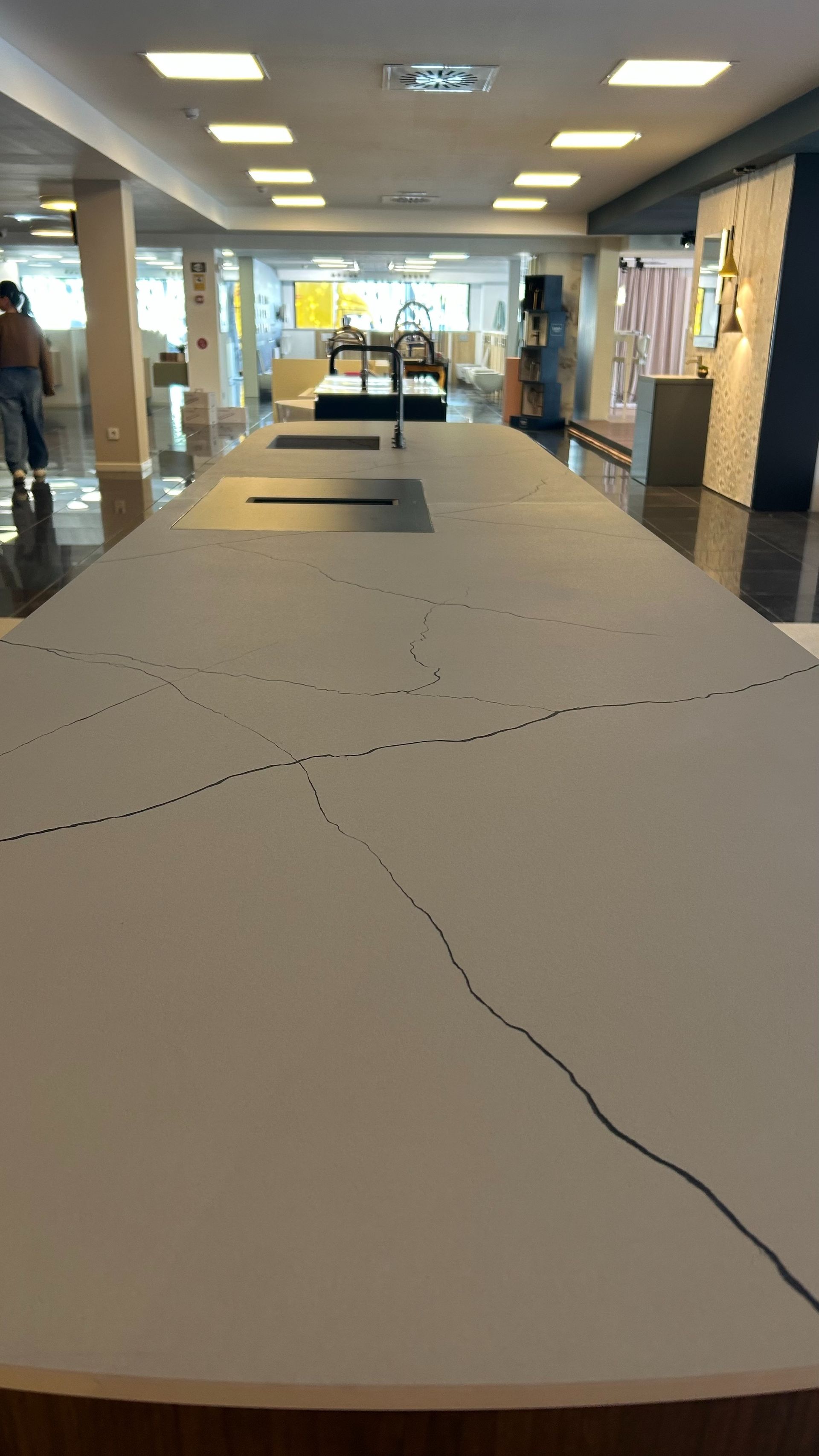 Encimera larga con vetas oscuras, en exposición con vitrinas de cocina e iluminación.