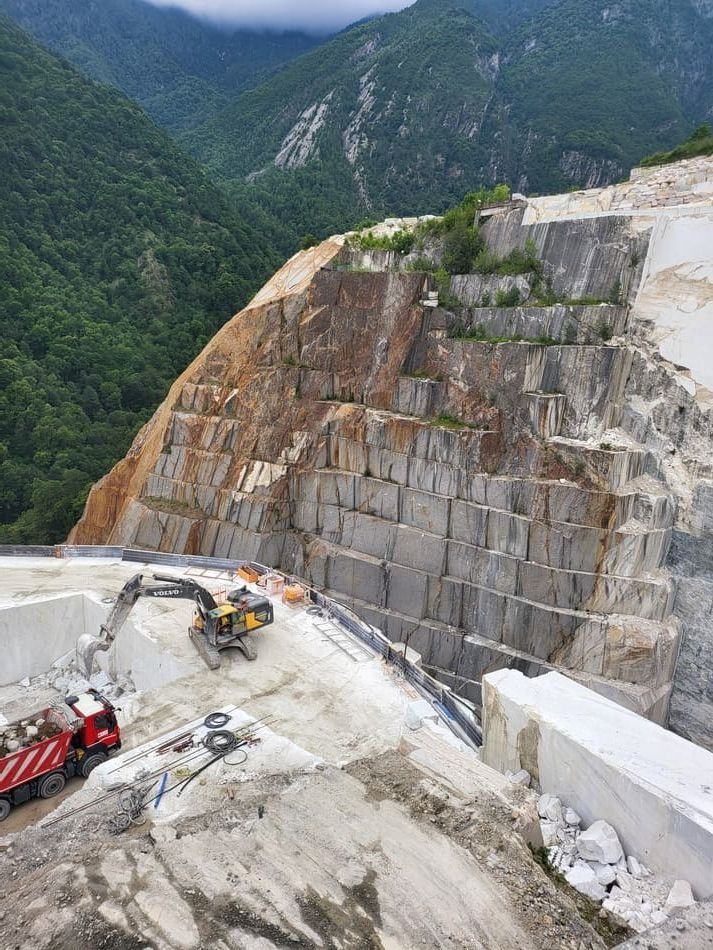 Cantera de mármol en montaña, con maquinaria pesada trabajando y bloques cortados.