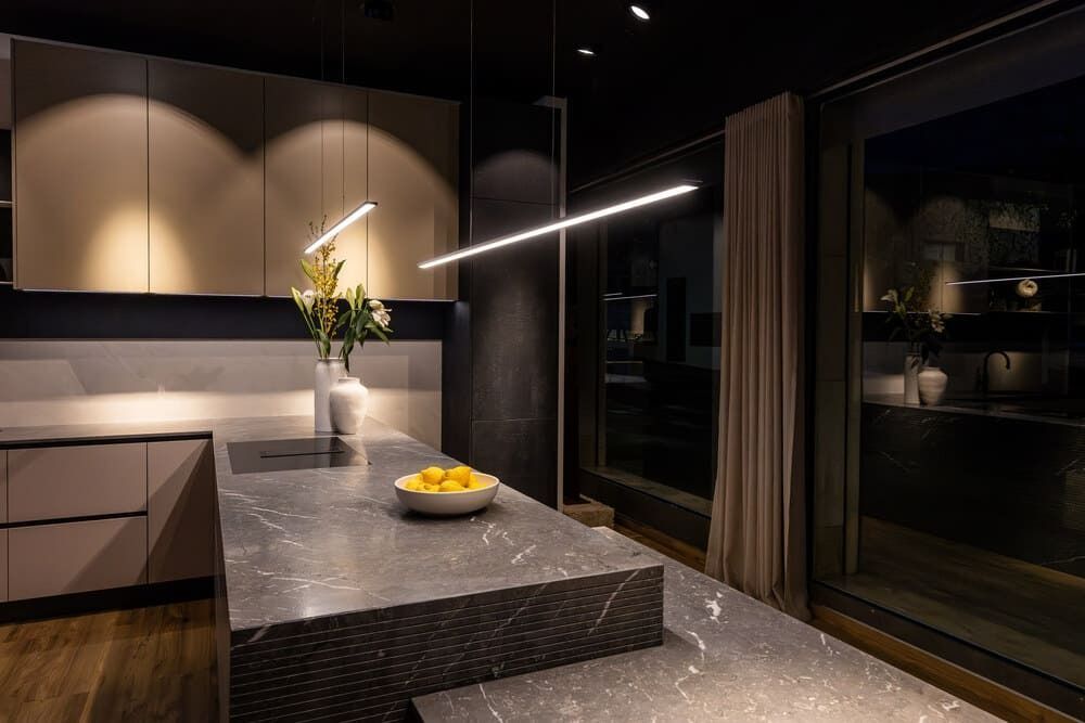 Cocina moderna con encimera oscura, iluminación cenital y limones en un bol.