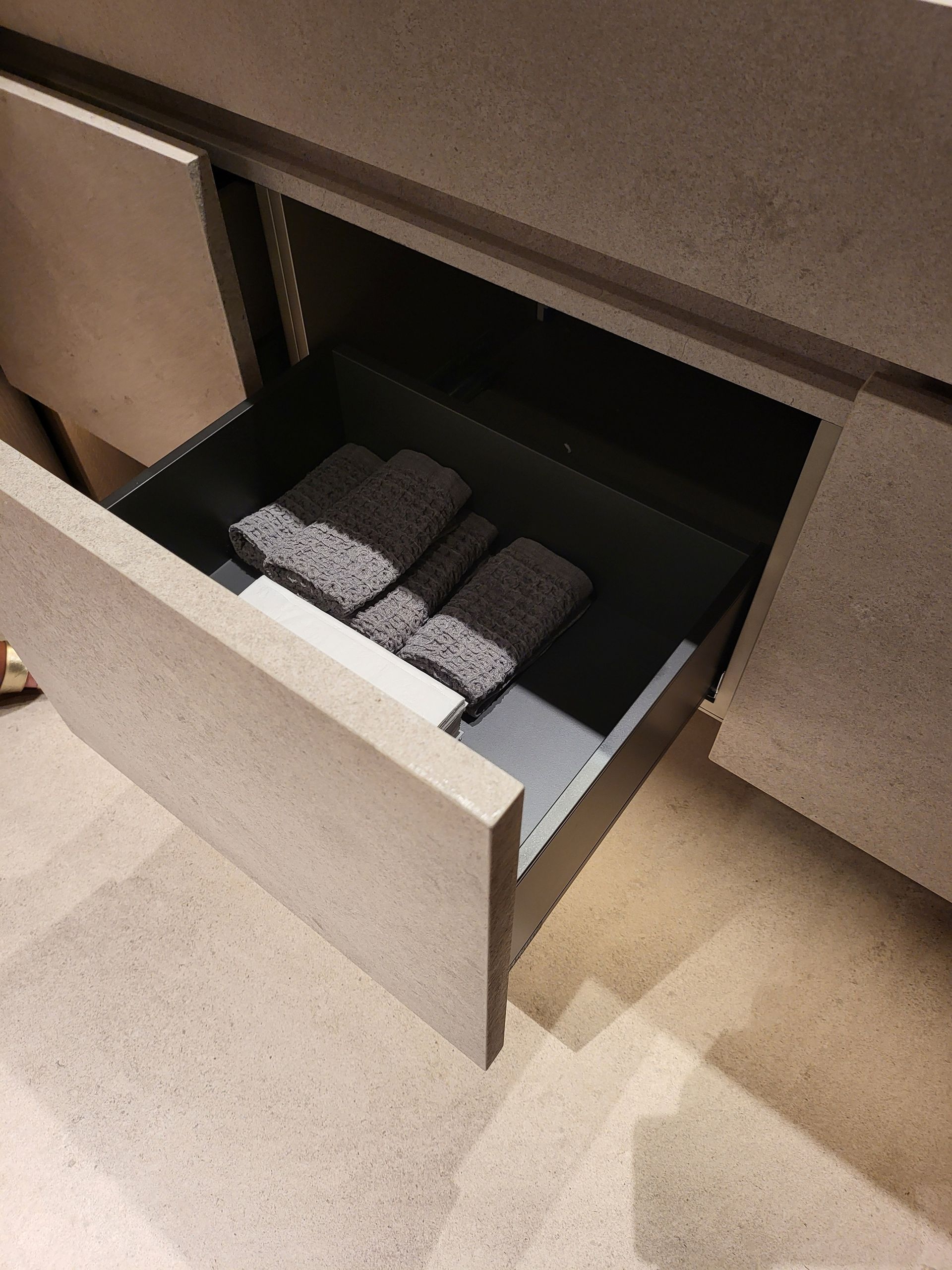 Cajón con toallas grises dentro de un mueble de color claro.