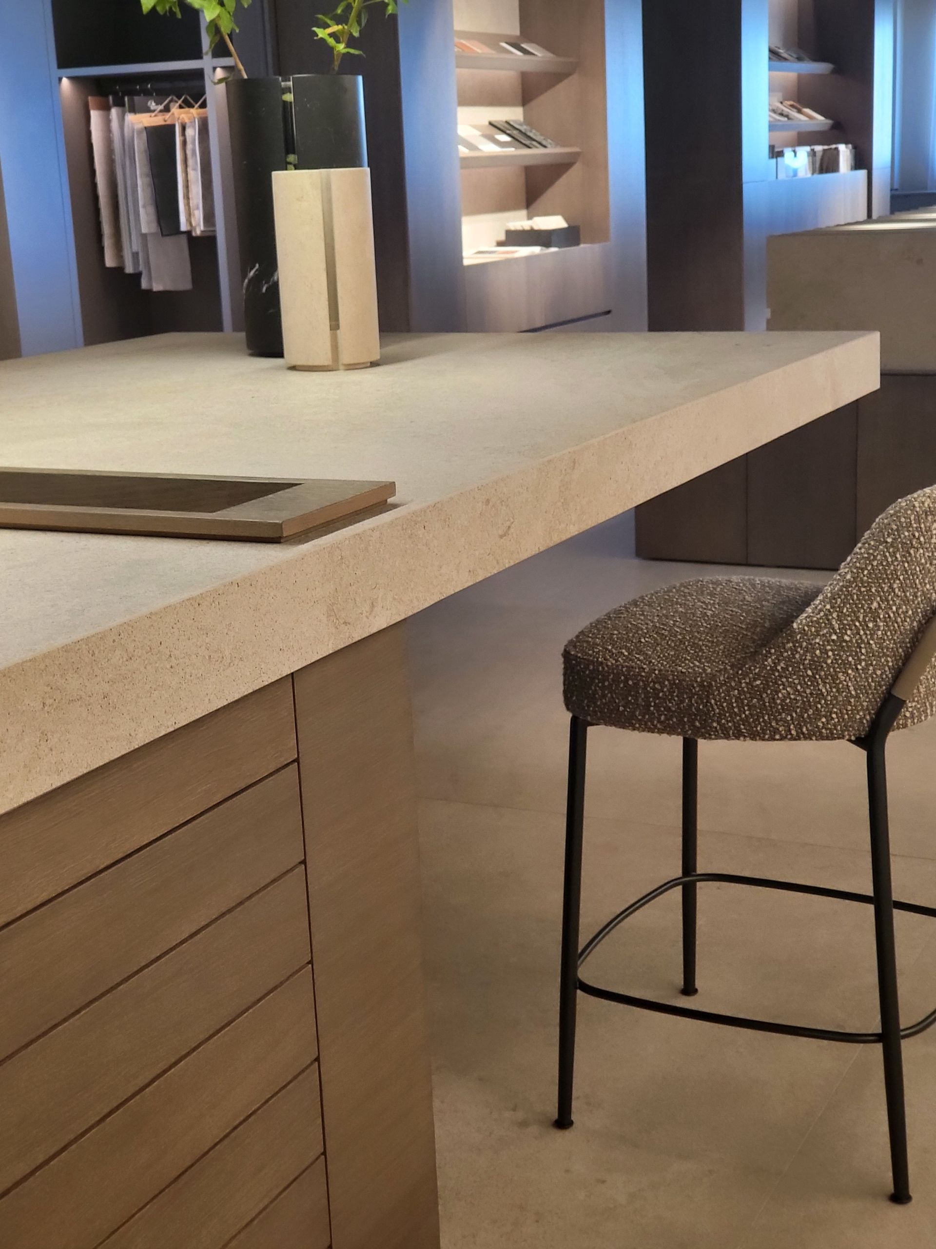 Una isla de cocina con encimera beige y paneles de madera, un taburete estampado y estanterías en el fondo.