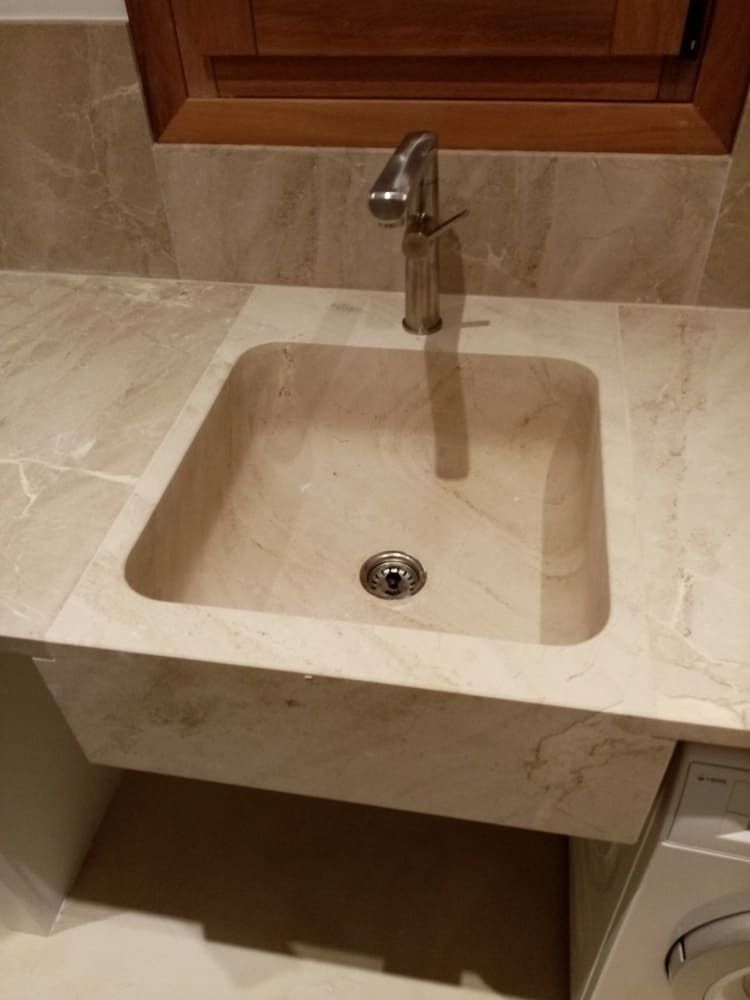 Lavabo de mármol beige con grifería cromada en un baño.