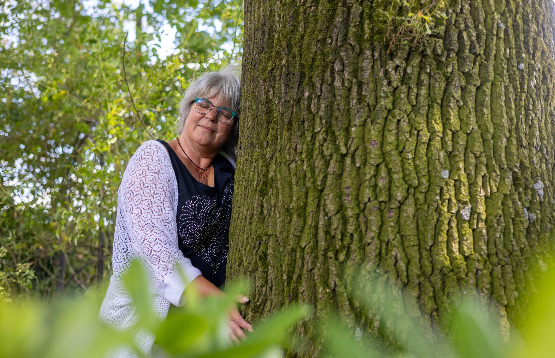 Eine Frau umarmt einen Baum im Wald.