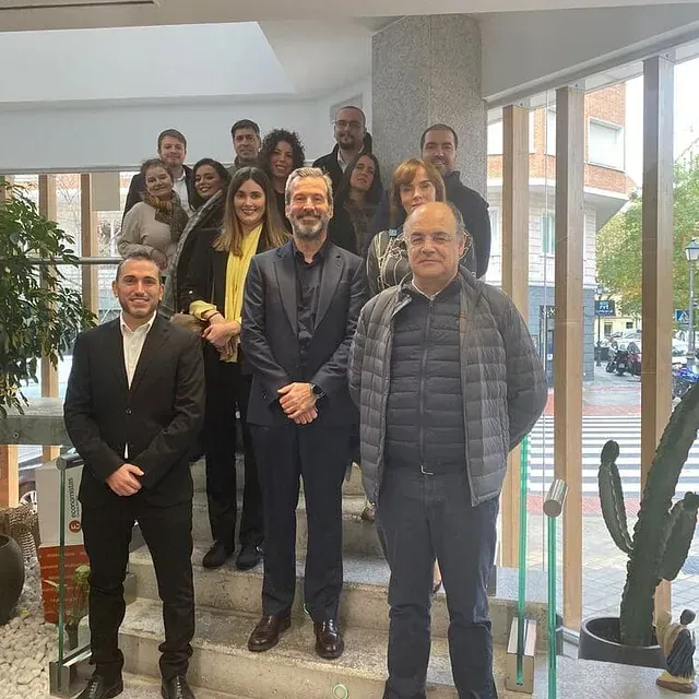 Grupo de personas posando en unas escaleras interiores con un cactus cerca y ventanas que dan al exterior.