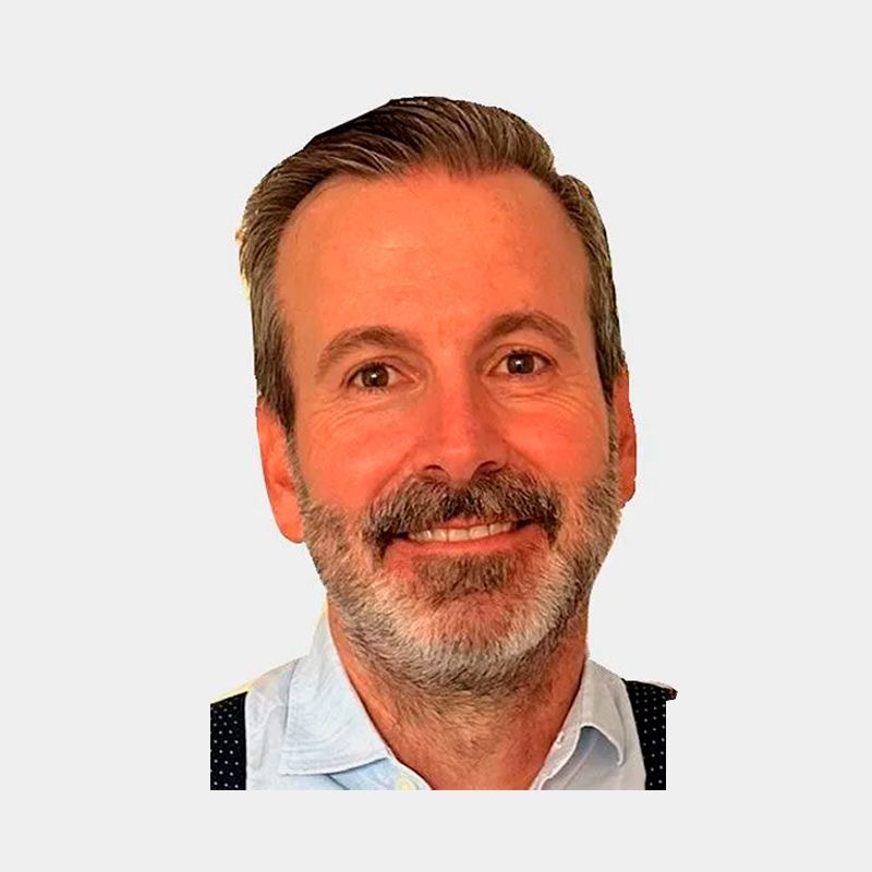 Hombre de ojos marrones, barba y sonriente; viste camisa azul claro y tirantes.