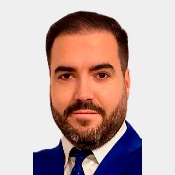 Hombre de ojos marrones, barba y sonriente; viste camisa azul claro y tirantes.