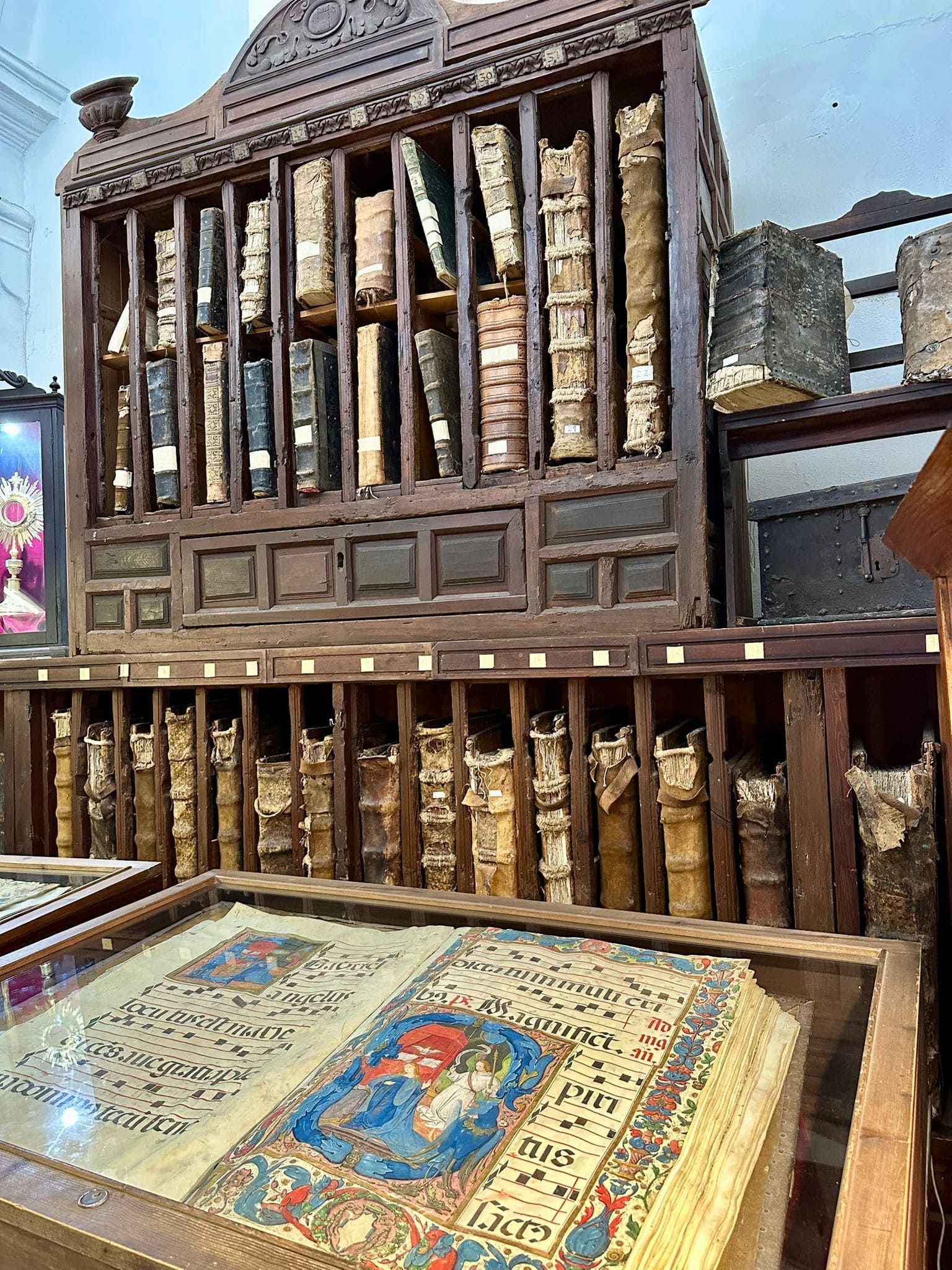 Estantería de madera repleta de libros antiguos y manuscritos iluminados en vitrinas.