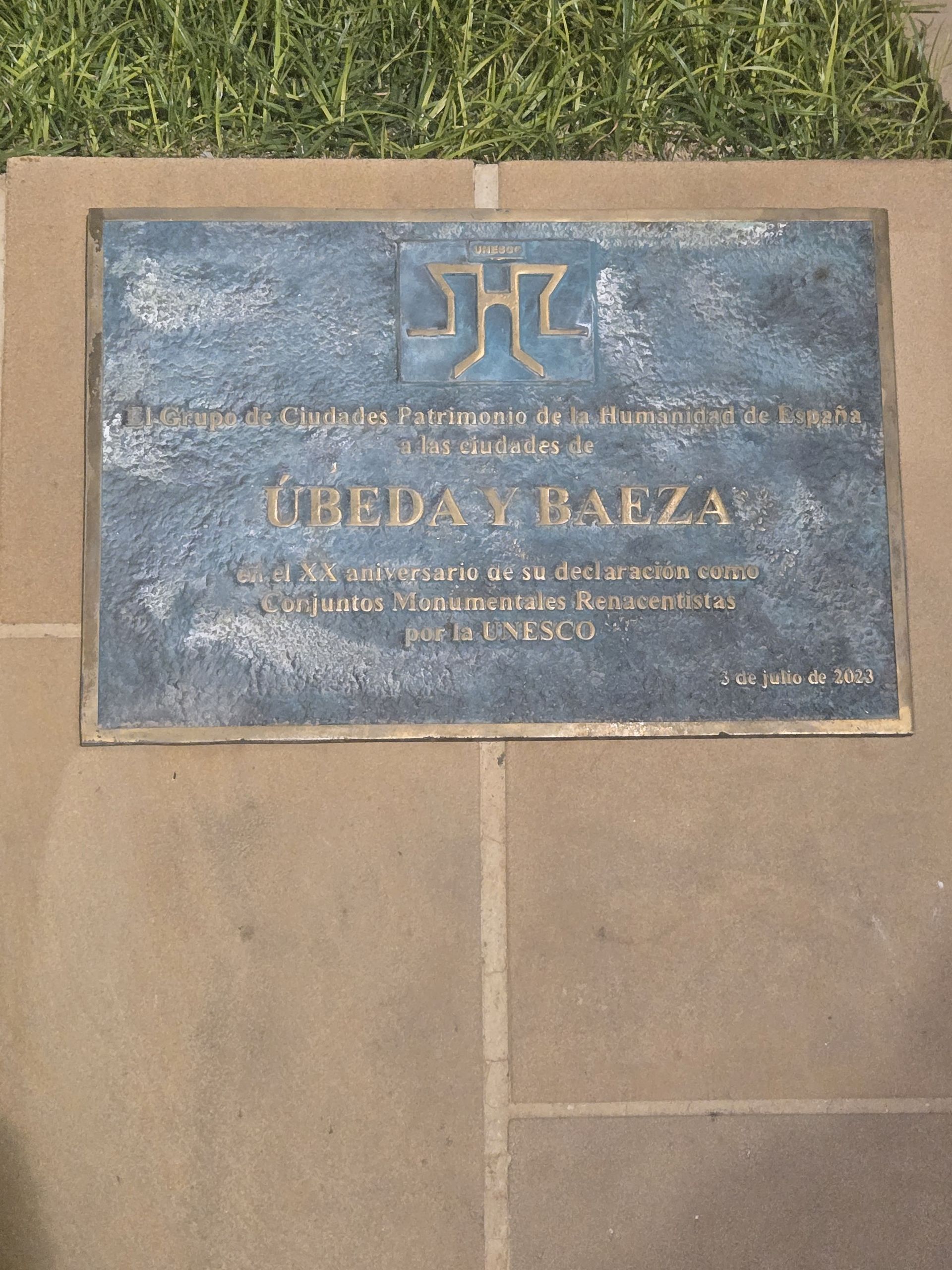 Placa de bronce incrustada en piedra; texto en español, con un símbolo encima del nombre 