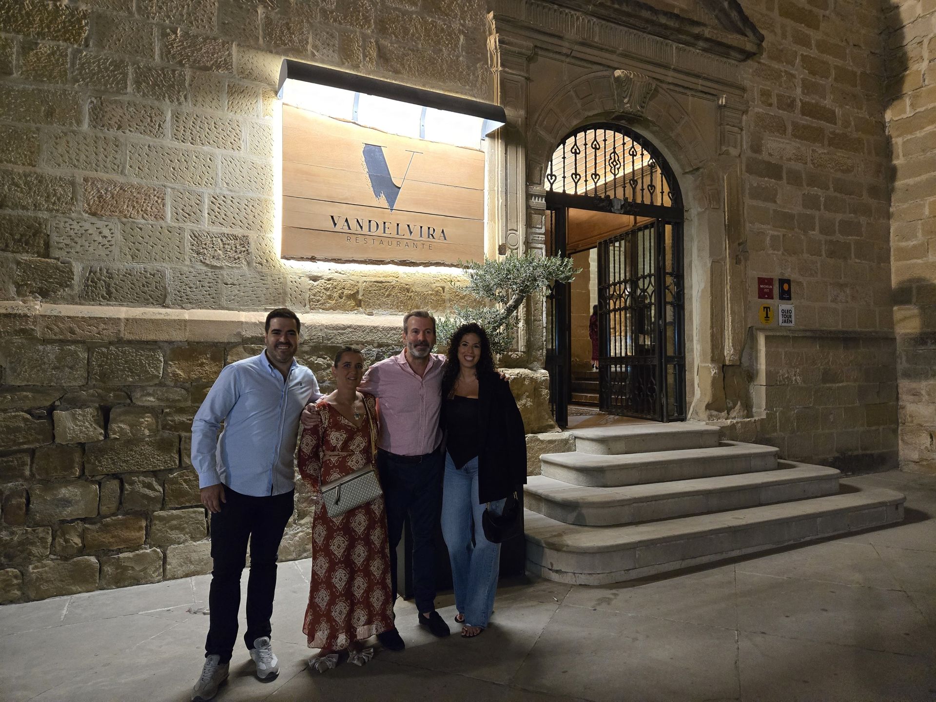 Cuatro personas posan frente a un edificio por la noche. El edificio tiene un letrero luminoso.