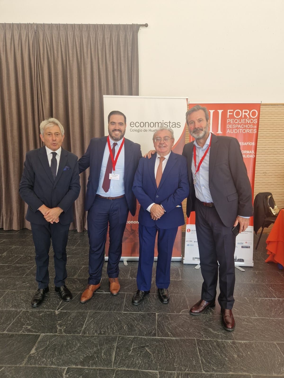 Cuatro hombres de traje posan delante de una pancarta en un evento.