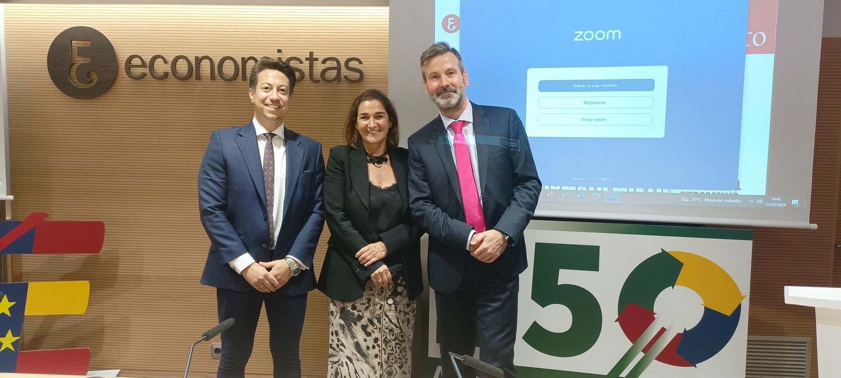 Tres personas de pie frente a una pantalla de presentación, una pared con un logotipo y un letrero con el número 
