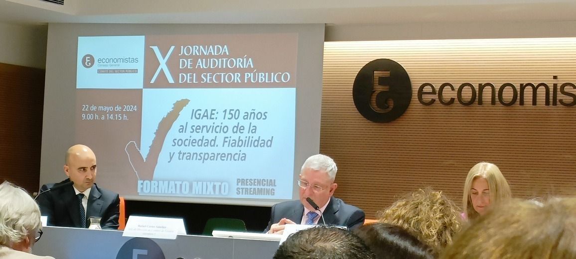 Mesa redonda en una conferencia. Los ponentes están sentados a una mesa frente a una pantalla. Logotipo de 