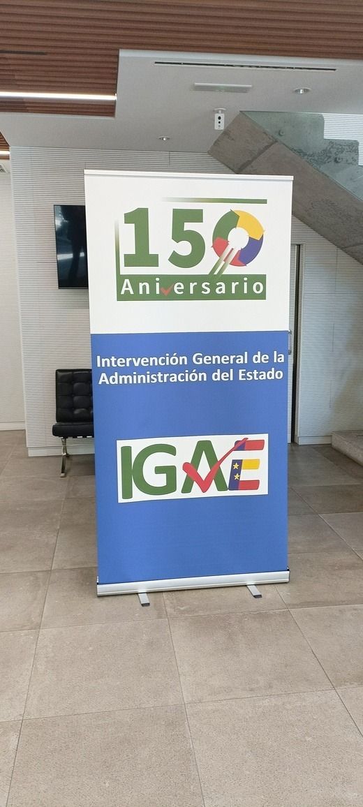 Pancarta conmemorativa del 150 aniversario, con la parte inferior azul y las letras IGME y otros textos. Entorno interior.