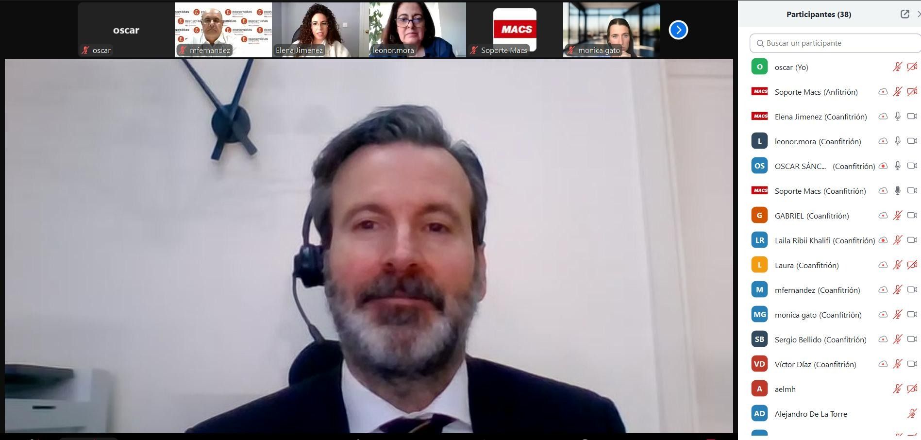 Hombre con traje negro y auriculares en una videollamada. Los participantes son visibles en la fila superior.