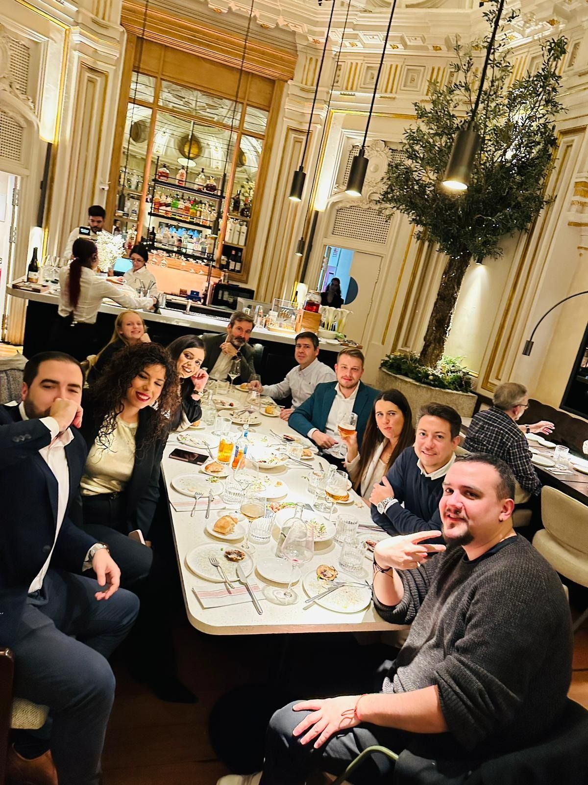 Personas sentadas a una mesa larga en un restaurante elegante, sonriendo y mirando a la cámara.