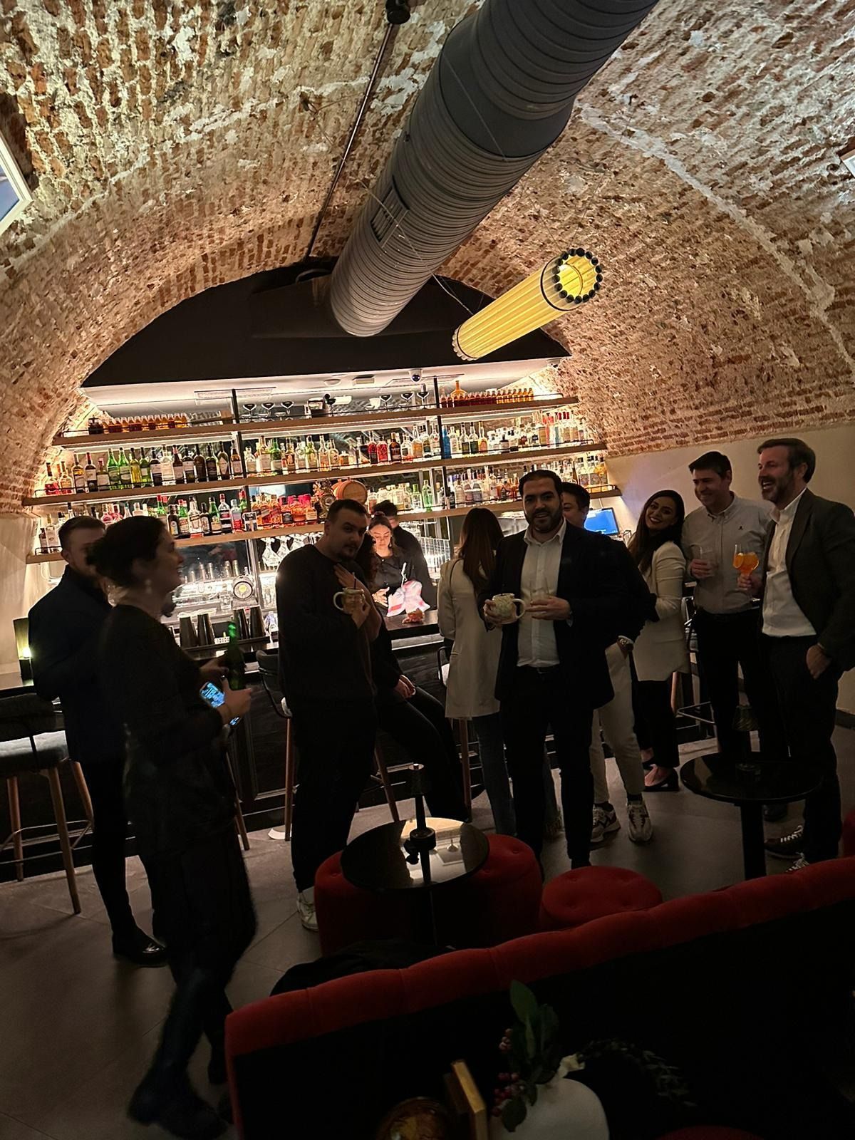 La gente se reunía en un bar con techo abovedado de ladrillo; un camarero detrás de la barra; iluminación tenue.