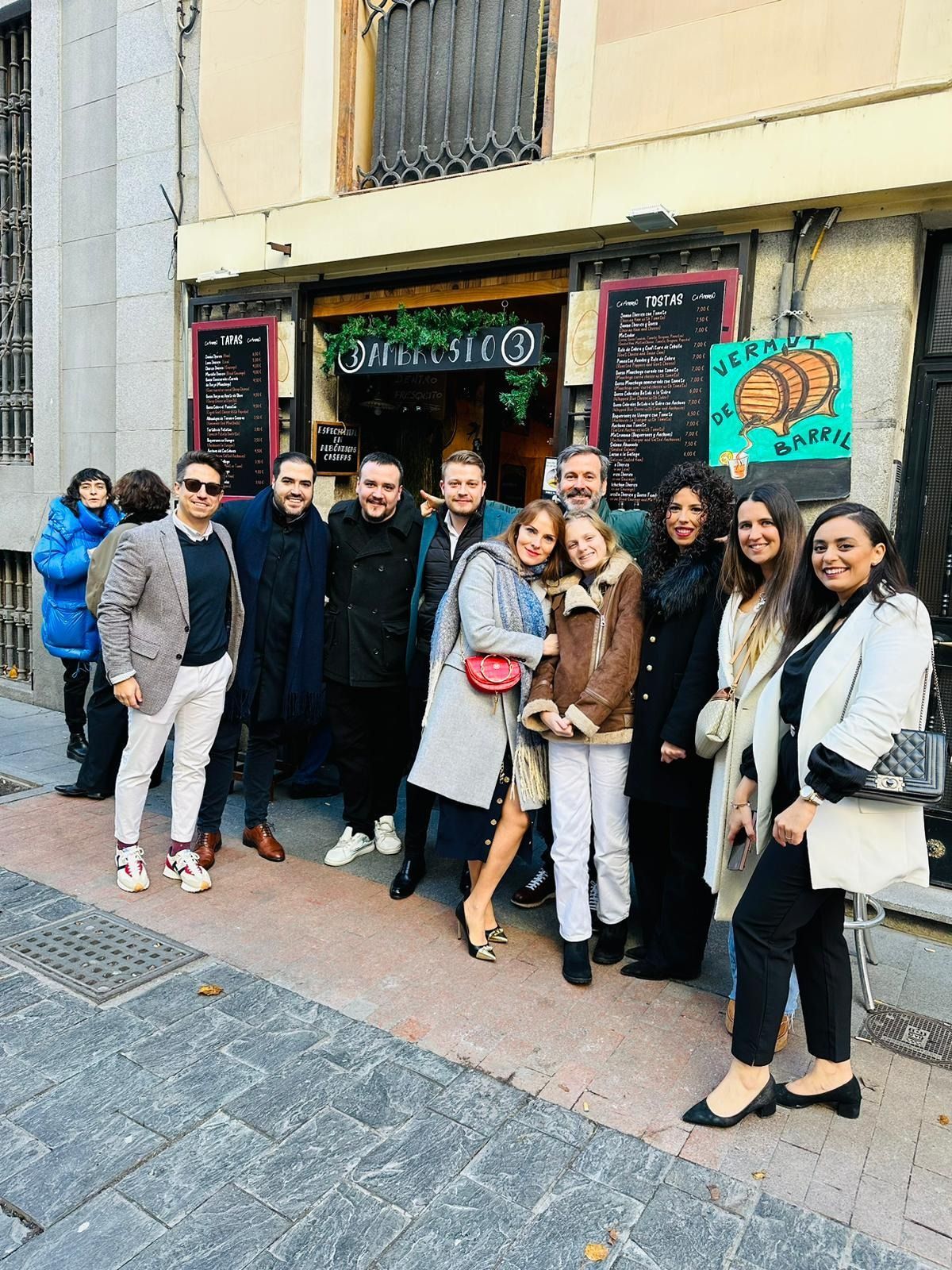 Grupo de personas posando delante de un bar con un letrero verde y barriles de madera en Madrid.