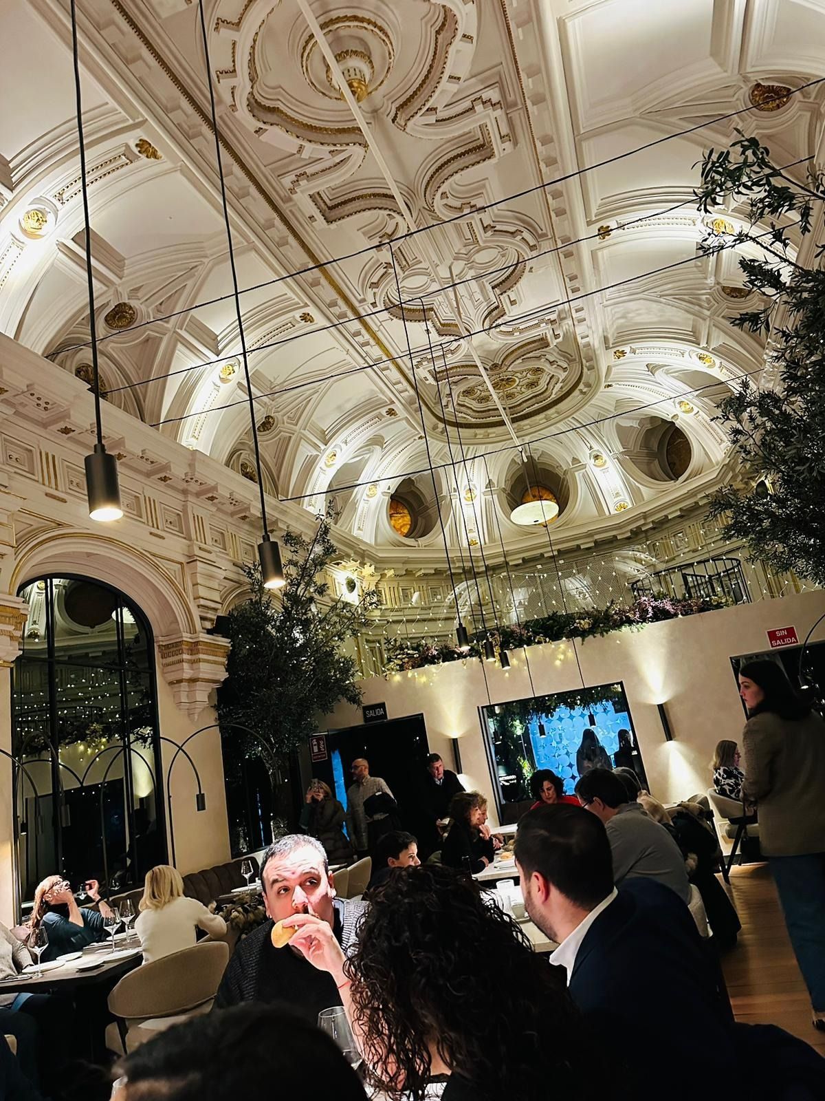 Interior del restaurante con techo ornamentado, gente comiendo y luz ambiental.