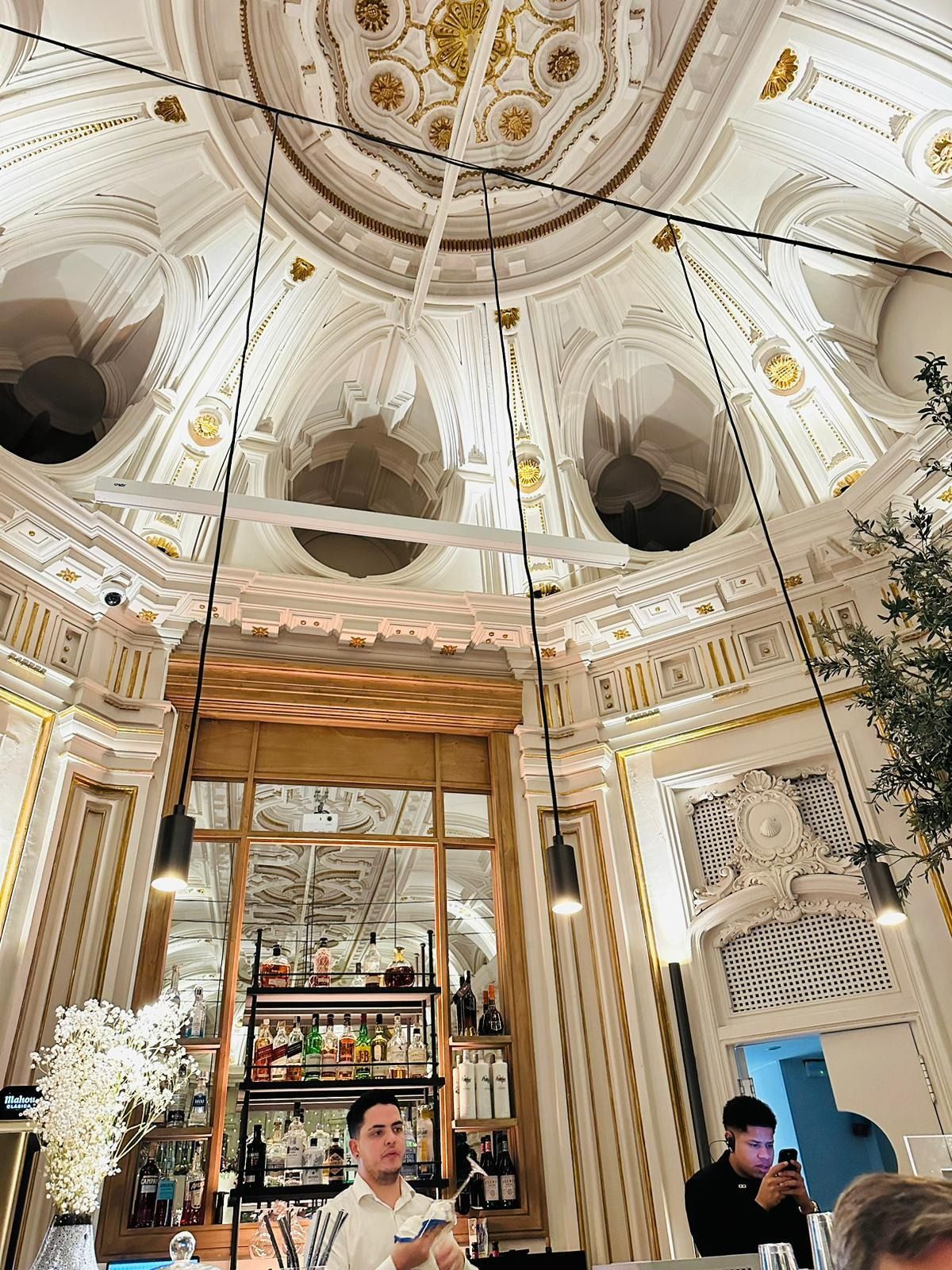 Techo blanco ornamentado con detalles dorados sobre una barra; dos personas presentes.