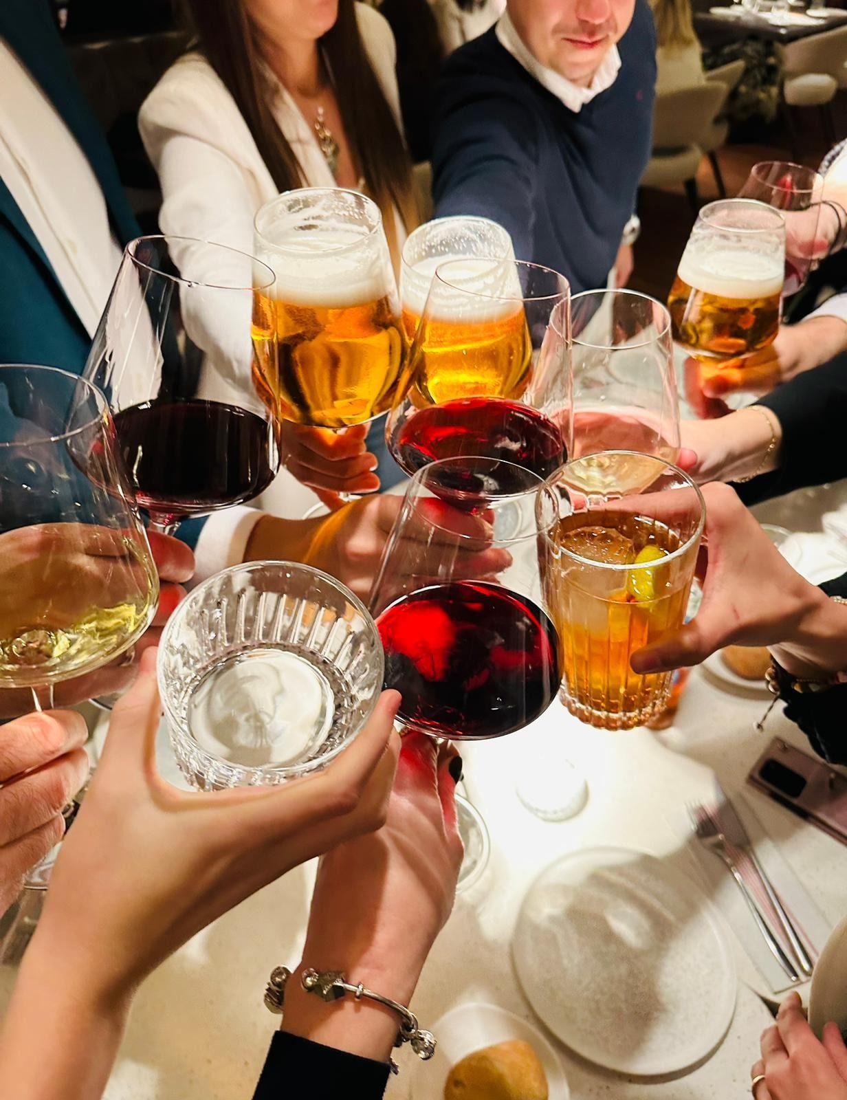 Personas brindando con diversas bebidas en la mesa de un restaurante: cerveza, vino y cócteles.