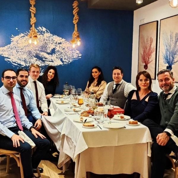 Grupo de personas sentadas a una mesa en un restaurante. Sonríen, con una pared decorada en azul y obras de arte.