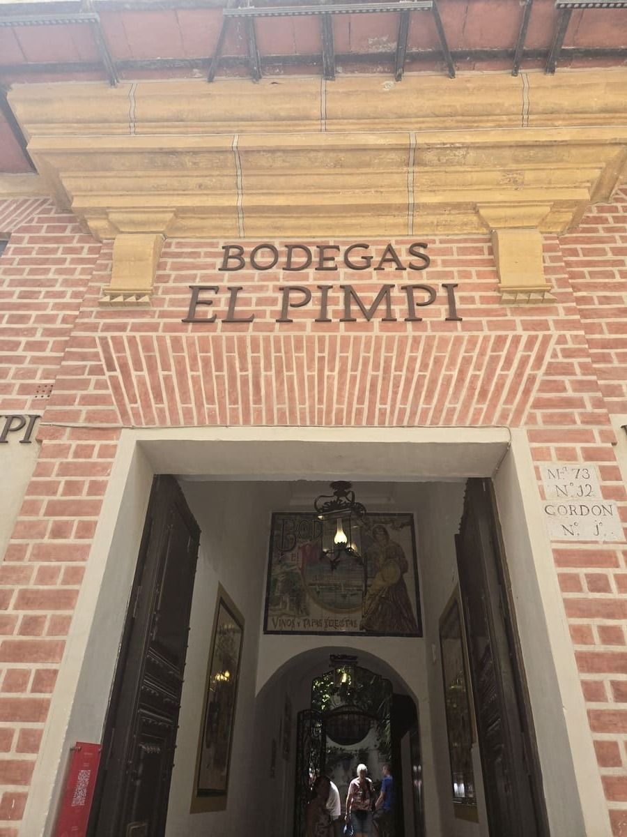 Entrada a Bodegas El Pimpi en Málaga, España. Fachada de ladrillo rojo, puerta arqueada con letrero.