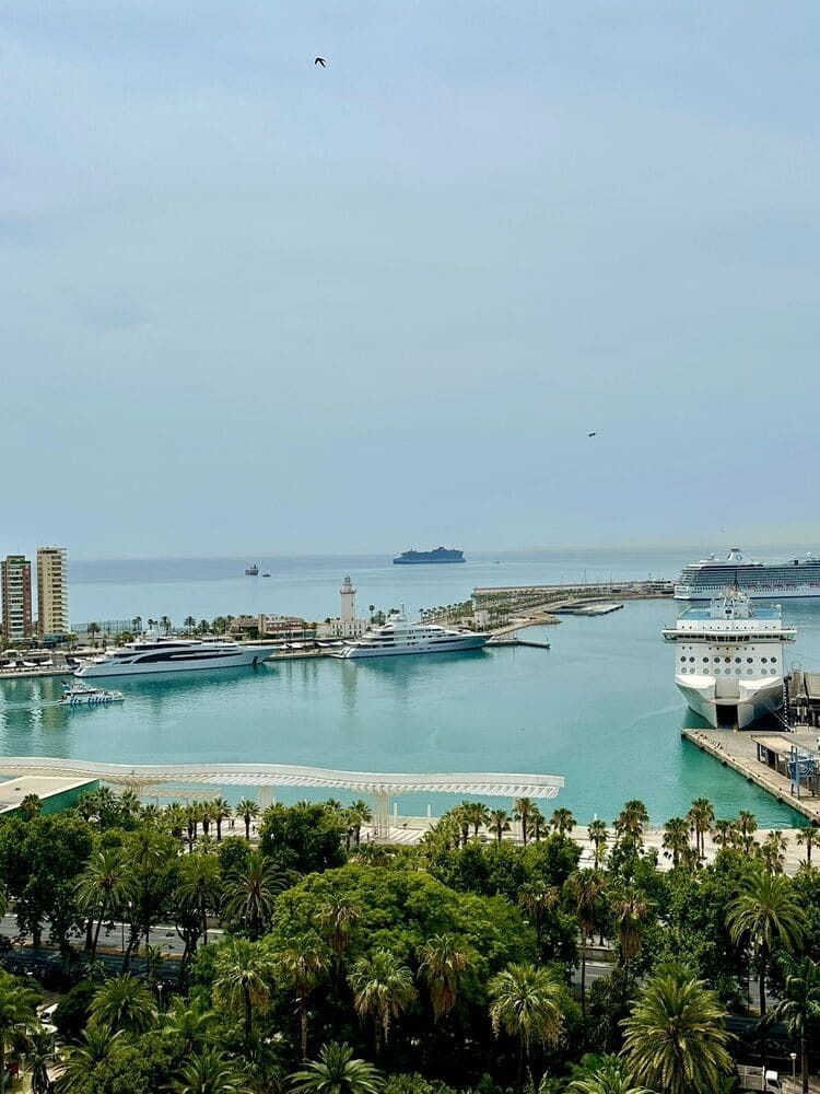 Vista del puerto con barcos, faro, agua turquesa y cielo despejado en Málaga, España.