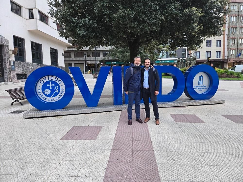 Dos hombres posan delante del cartel azul 