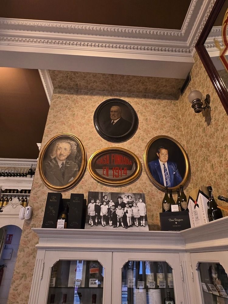 Una pared con retratos enmarcados de figuras notables sobre un armario, en una habitación con papel pintado estampado.