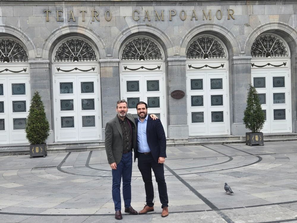 Dos hombres posan frente al Teatro Campoamor. El edificio tiene puertas arqueadas y ventanas ornamentadas.