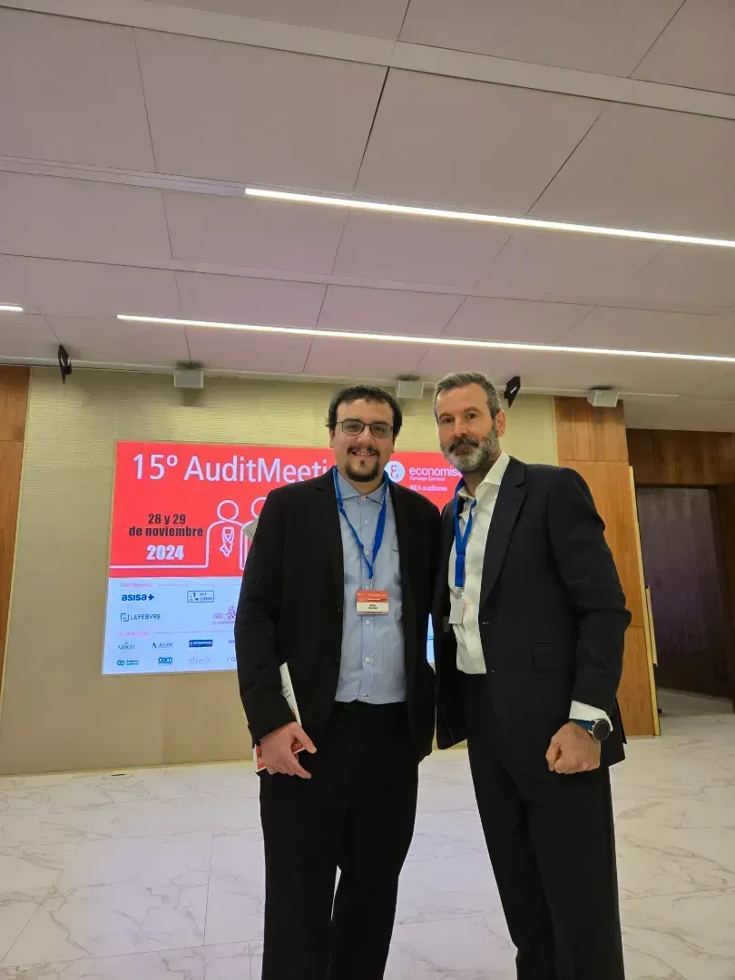 Dos hombres con traje están de pie frente a una pantalla de conferencias, sonriendo.