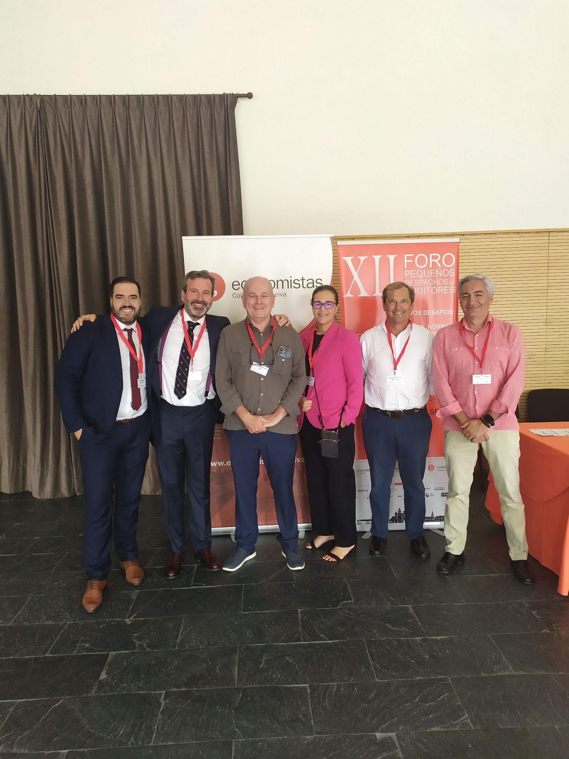 Grupo de personas posando juntas en un evento, con una pancarta y una cortina de fondo.
