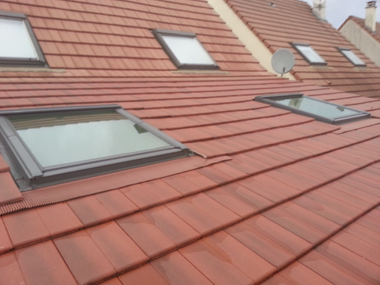 Maison avec toit de tuiles rouges, puits de lumière et antenne parabolique.