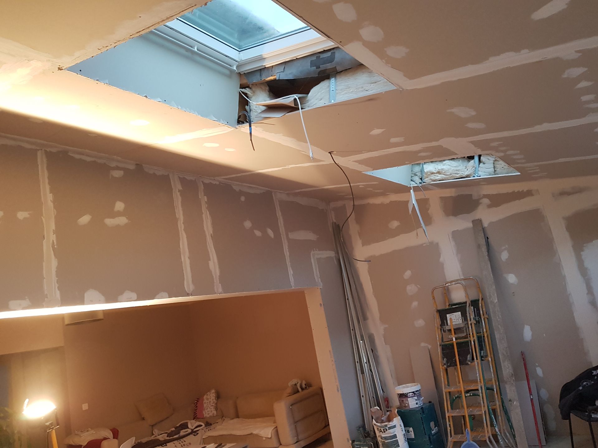 Pièce inachevée avec cloisons sèches, ouvertures au plafond, une échelle et des outils en cours de rénovation.