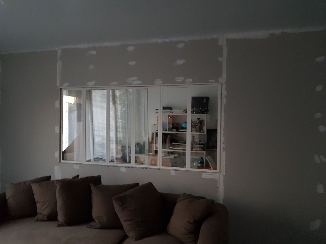Grenier vide avec plafond en bois incliné, puits de lumière, murs blancs et poutre de soutien noire.