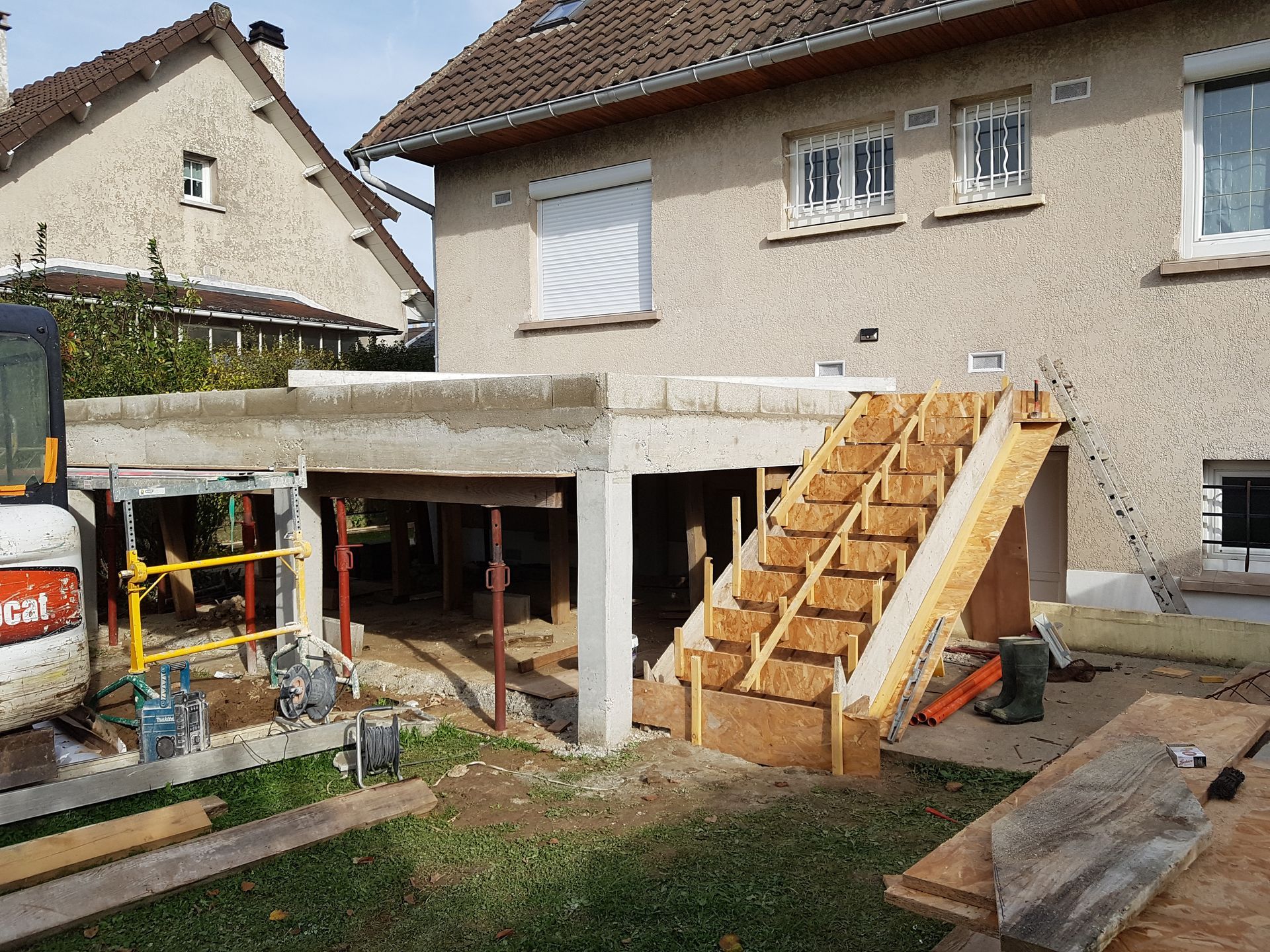 Chantier de rénovation avec échelles, outils et murs non finis dans une pièce nue.