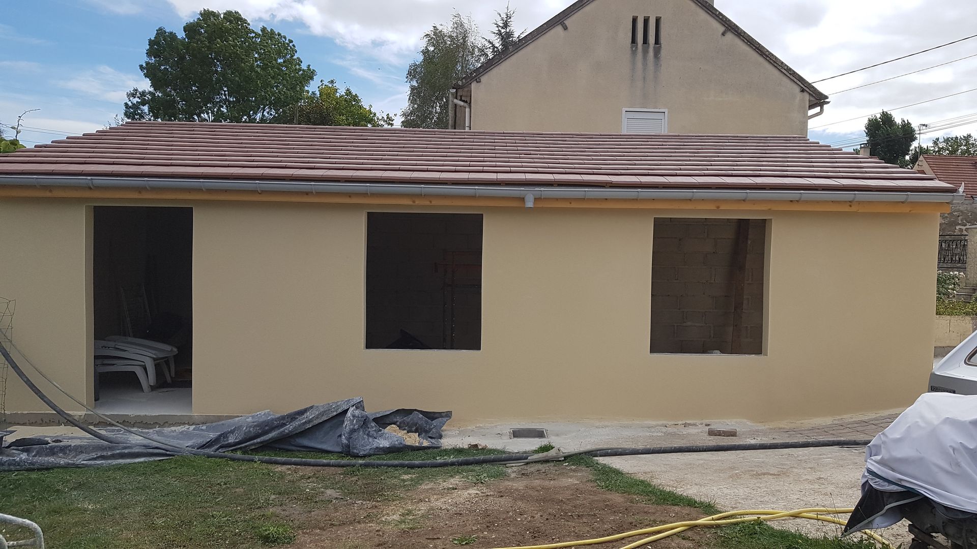 Maison beige de plain-pied avec un toit marron et des fenêtres condamnées, en cours de rénovation.