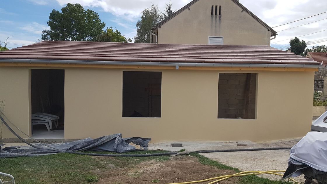 Façade de maison moderne avec un portail coulissant en métal gris foncé et des murs blancs sous un ciel nuageux