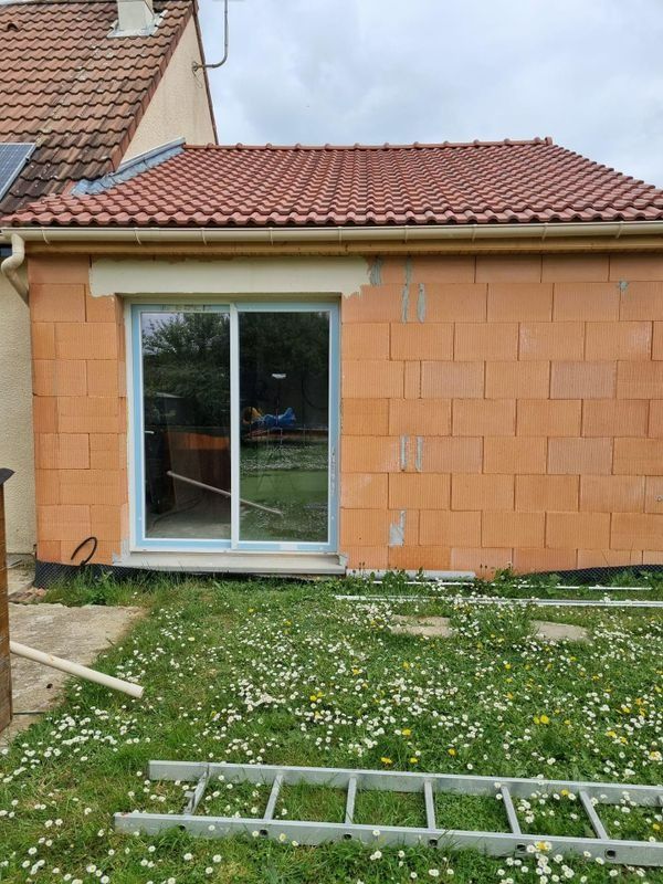 Vue arrière d'une maison avec une porte coulissante en verre, un mur orange, un toit rouge et une échelle sur la pelouse.