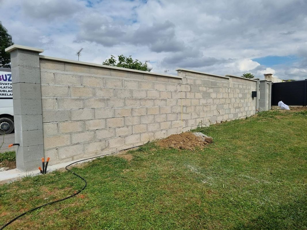 Mur en parpaings le long d'une pente herbeuse sous un ciel nuageux.