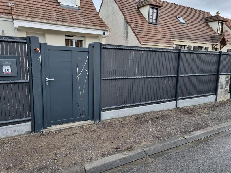 Portail et clôture gris foncé devant des maisons de banlieue le long d'une rue.
