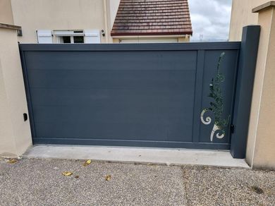 Portail d'allée en métal gris foncé avec une vigne sur le côté droit, encastré dans un mur en stuc.