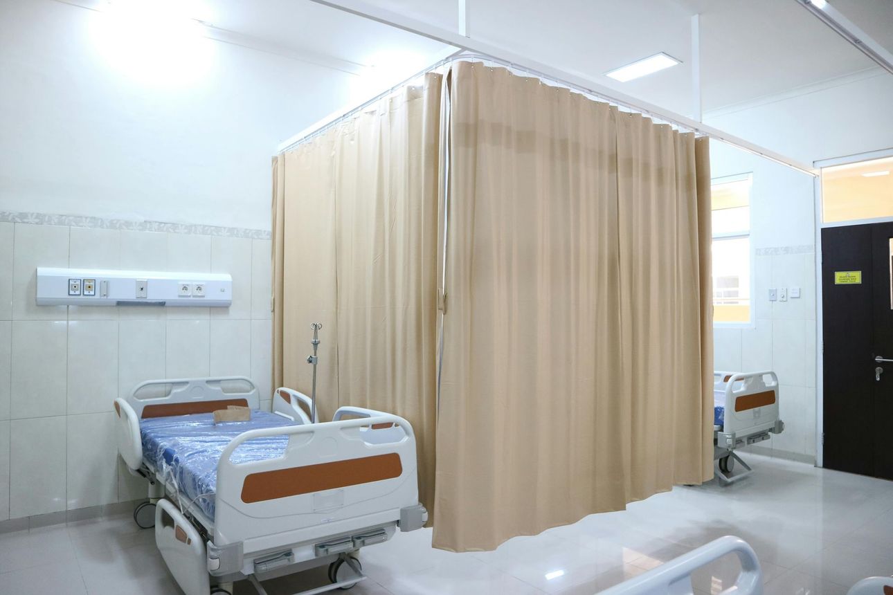 Habitación de hospital con dos camas separadas por una cortina beige.
