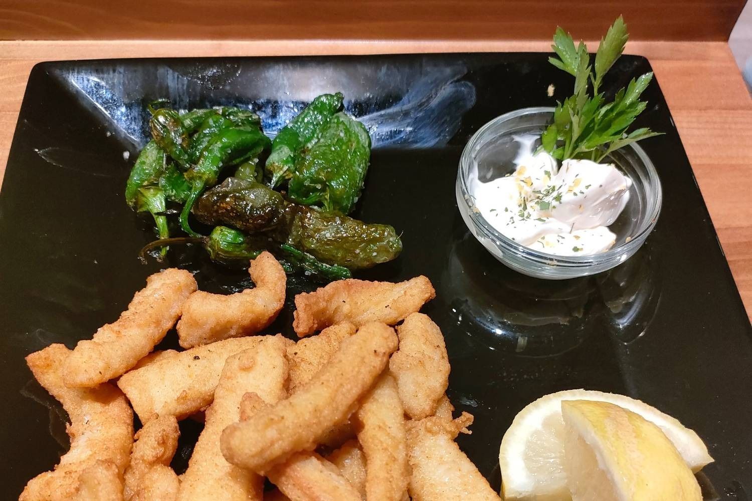 Un plato negro cubierto con comida frita y una rodaja de limón.