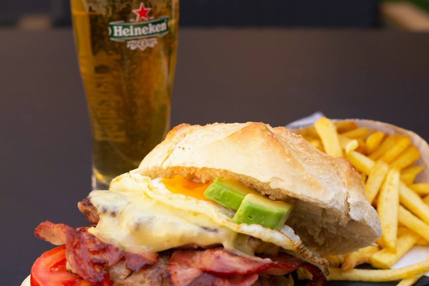 Una hamburguesa y papas fritas junto a un vaso de cerveza Heineken