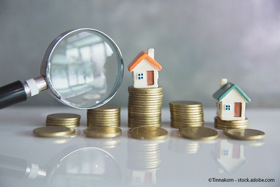 Lupe neben Münzgeldstapeln mit Miniaturhäusern