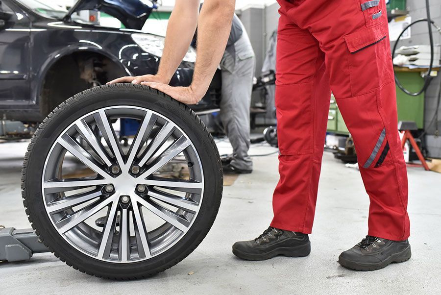 Ein Mann in roten Hosen montiert einen Reifen auf eine Autofelge.