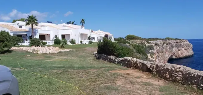 Villas blancas junto al mar, al lado de un acantilado cubierto de hierba y el océano azul bajo un cielo despejado.