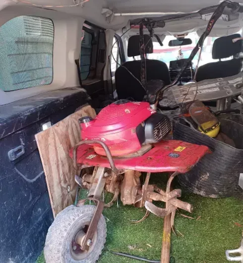 Una cortadora de césped roja con asiento, cargada dentro de una furgoneta, con tablones de madera