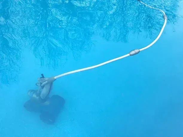 Una persona sumergida en una piscina azul, ajustando una manguera o cable blanco cerca de la superficie.